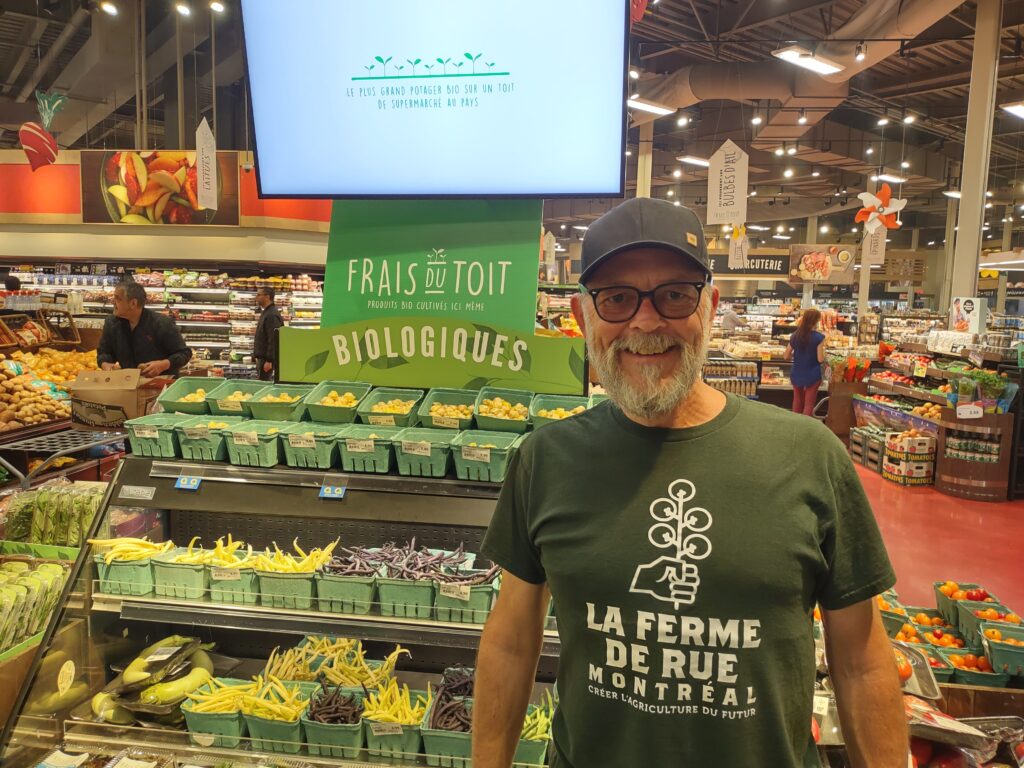 Réal Migneault devant les étals d'épicerie avec les produits cultivés sur le toit de l'épicerie. 